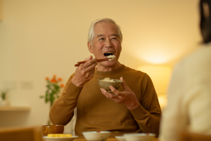 入れ歯を入れて美味しく食事をする高齢男性