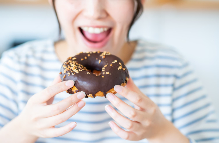 前歯の虫歯の原因になる甘いドーナツを食べる女性